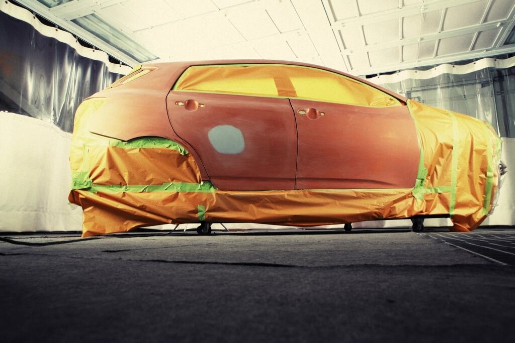 Een wagen in een spuitcabine, afgeplakt met papier en tape, met een nieuwe grondlaag op het portier.